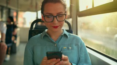 Toplu taşıma. Tramvaydaki gözlüklü kadın akıllı telefon konuşmaları yapıyor ve arkadaşlarıyla mesajlaşıyor. Şehir, şehir, ulaşım. Yavaş çekim