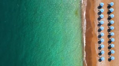 Mavi güneş şemsiyeleri ve turkuaz deniz suyuyla cennet gibi kumlu sahil manzarası.. 