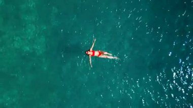 Kırmızı mayo giymiş bir kadının havadan görünüşü, kristal berrak deniz sularında rahatlama somutlaştırıcı bir şekilde zahmetsizce sırt üstü yüzüyor. Yaz tatilleri.