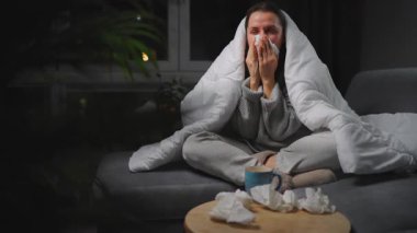 Hasta kız grip olmuş ya da nezle olmuş, alerji belirtileri gösteriyor. Alerjisi olan genç bir kadın mendil içinde hapşırıyor, burnunu siliyor ve çay içiyor. Sağlıksız kadın mevsimsel virüs hastalığından muzdarip..