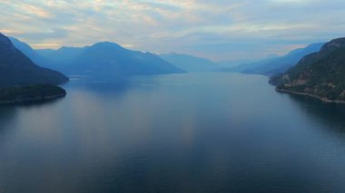 Akşamları Vancouver 'ın kuzeyindeki deniz manzarası. Gün batımı bulutlu gökyüzü ve dağların siluetleri. British Columbia, Kanada.
