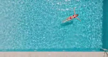 Kırmızı mayo giymiş bir kadının havuzda sırt üstü yatışı. Kamera yükseliyor. Rahatlatıcı konsept, yaz yaşam tarzı