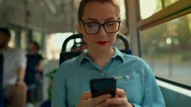 Toplu taşıma. Tramvaydaki gözlüklü kadın akıllı telefon konuşmaları yapıyor ve arkadaşlarıyla mesajlaşıyor. Şehir, şehir, ulaşım. Yavaş çekim