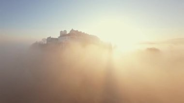 Polonya 'nın Tyniec kentindeki Vistula Nehri ve Benedictine Manastırı' nın alışılmadık hava manzarası. Güneş ışınları sabah sisinin içinden geçiyor. Katolik manastırı ve çevresindeki manzaranın eski mimarisi. Kaydedildi