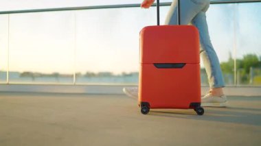 Bir gezgin gün batımında şık kahverengi bavullarıyla havaalanı terminalinde rahatça dolaşır. Yaz tatili kavramı.