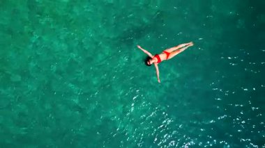 Kırmızı mayo giymiş bir kadının hava görüntüsü, kristal berrak deniz sularında rahatlama somutlaştırıcı bir şekilde sırtüstü uzanır. Yaz tatilleri.