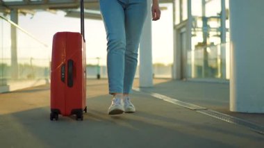 Bir gezgin gün batımında şık kahverengi bavullarıyla havaalanı terminalinde rahatça dolaşır. Yaz tatili kavramı.