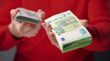 Bir adam Amerikan doları ve avrosunu elinde tutuyor ve hangi seçeneğin daha iyi olduğunu seçiyor. Yatırım, başarı, finansal beklentiler veya kariyer ilerlemesi kavramı.