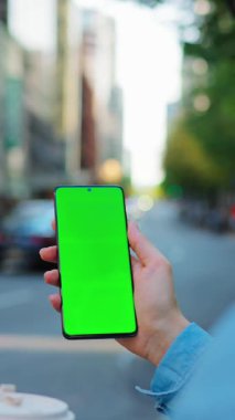 Kadın sokakta dikiliyor ve yeşil ekranlı, arka görüşlü akıllı telefon kullanıyor. İletişim, iş günü, yoğun yaşam konsepti. Yavaş çekim