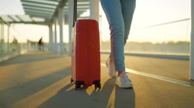 Bir gezgin gün batımında şık kahverengi bavullarıyla havaalanı terminalinde rahatça dolaşır. Yaz tatili kavramı.