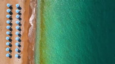 Mavi güneş şemsiyeleri ve turkuaz deniz suyuyla cennet gibi kumlu sahil manzarası..