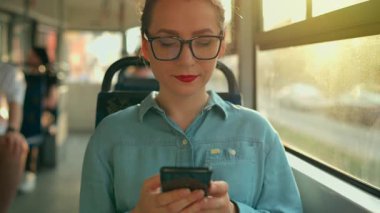 Toplu taşıma. Tramvaydaki gözlüklü kadın akıllı telefon konuşmaları yapıyor ve arkadaşlarıyla mesajlaşıyor. Şehir, şehir, ulaşım. Yavaş çekim