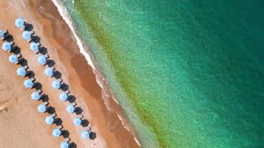 Mavi güneş şemsiyeleri ve turkuaz deniz suyuyla cennet gibi kumlu sahil manzarası..