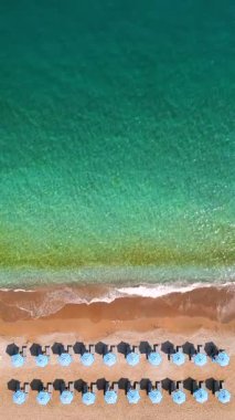 Mavi güneş şemsiyeleri ve turkuaz deniz suyuyla cennet gibi kumlu sahil manzarası..