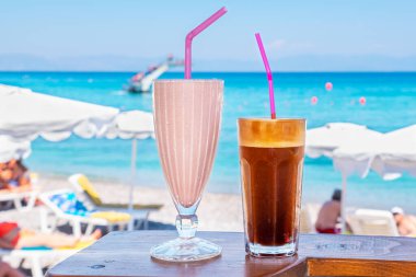 Glasses with milkshake and frappe on a table with view of the beach. Rhodes, Greece