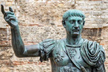 Bronze statue of Roman Emperor Trajan before remains of London Wall. London, England