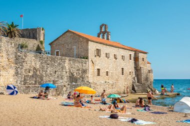 Budva, Montenegro - July 7, 2023: People relaxing on the beach near wals of old town clipart