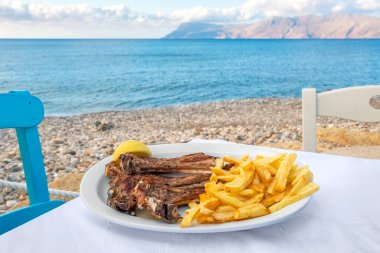 Grilled lamb ribs with fries on a table in seaside tavern. Crete, Greece. clipart