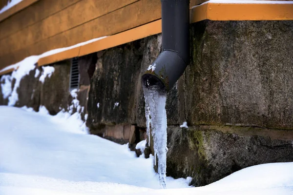 冬天在一座老房子的石基附近有冰冷的排水管道 免版税图库图片