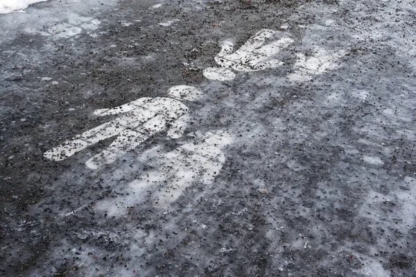 Ice covered sidewalk with a pedestrian path sign sprinkled with granite chips