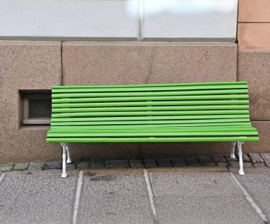 Helsinki, Finlandiya 'da bir evin granit temelinin yanındaki granit kaldırımda parlak yeşil bir bank.