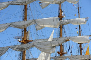 A detailed close-up view of the intricate rigging, masts, and sails of a tall ship. The image captures a complex web of ropes, pulleys, and lines against a background of clear sky and some signal flags. The focus is on the ship's rigging system, show clipart