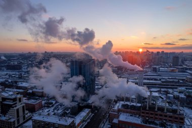 Mavi kış günbatımına karşı buhar bulutu olan büyük eski bir borunun silueti. Büyük bir kazan dairesi tam kapasite çalışıyor.