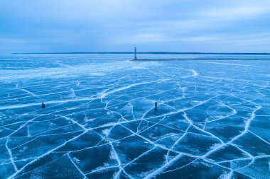 Donmuş göl, çatallı mavi buz. Balıkçılar avlanıyor, arkasında baraj olan bir deniz feneri.