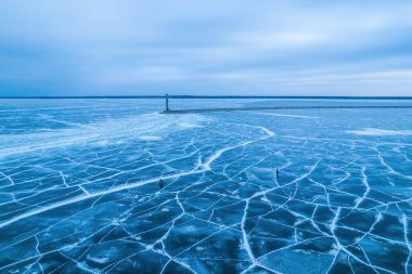 Donmuş göl, çatallı mavi buz. Balıkçılar avlanıyor, arkasında baraj olan bir deniz feneri.