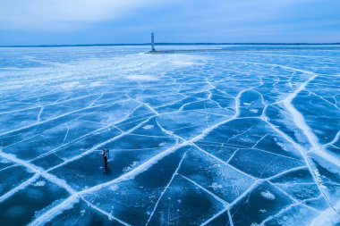 Donmuş denizdeki yalnız bir deniz fenerinin havadan görünüşü. Çatlaklarda donmuş mavi buz, drone görünümü