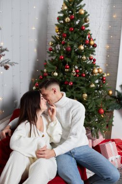 Aşk evde hediye ağacıyla yakınındaki Aralık ayında Noel arifesi öpüşme içinde genç tatlı güzel Çift.