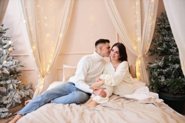 Genç çift Noel ağacının yanında poz veriyor ve sarılıyorlar.