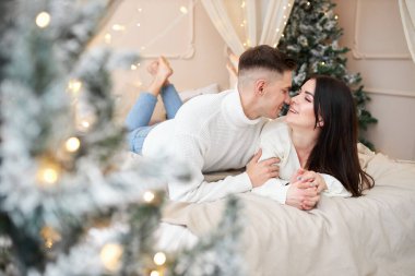 Aşk evde hediye ağacıyla yakınındaki Aralık ayında Noel arifesi öpüşme içinde genç tatlı güzel Çift.