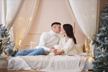 Genç çift Noel ağacının yanında poz veriyor ve sarılıyorlar.