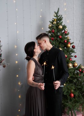 Aşk evde hediye ağacıyla yakınındaki Aralık ayında Noel arifesi öpüşme içinde genç tatlı güzel Çift.