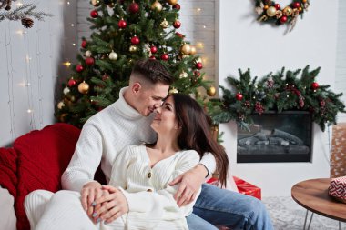 Aşk evde hediye ağacıyla yakınındaki Aralık ayında Noel arifesi öpüşme içinde genç tatlı güzel Çift.