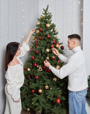 Genç çift Noel ağacının yanında poz veriyor ve sarılıyorlar.