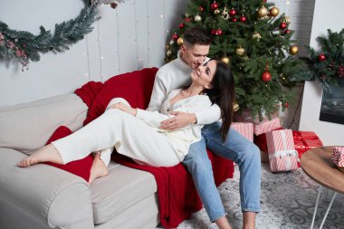 Genç çift Noel ağacının yanında poz veriyor ve sarılıyorlar.