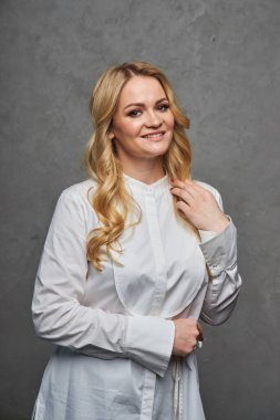 Stüdyo güzelliği, yaz elbisesi giymiş genç bir kadının portresi. Gri arka planda poz veren yazlık elbiseli sarışın kadın. Yüzüne yakın eli olan kız.