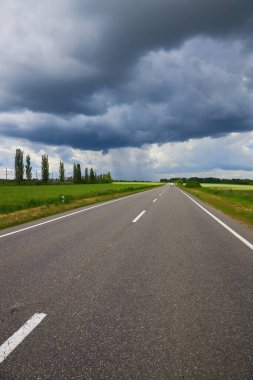 Empty highway, paved road through the fields. Dramatic sky, rain on the horizon in the distance. The storm is coming. Concept landscape.