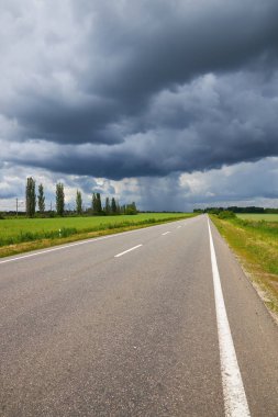 Empty highway, paved road through the fields. Dramatic sky, rain on the horizon in the distance. The storm is coming. Concept landscape.