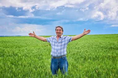 A Portrait of a happy farmer kneeling down in a wheat field with a beautiful landscape in the background