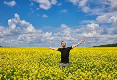 Attractive man with arms outstretched. Handsome young man standing in a field of blooming yellow rapeseed flowers.