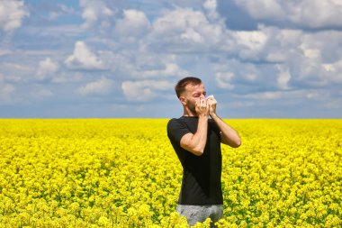 man in field blowing his nose and suffering from hay fever. Allergy