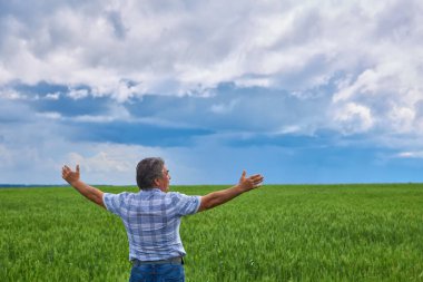 A Portrait of a happy farmer kneeling down in a wheat field with a beautiful landscape in the background