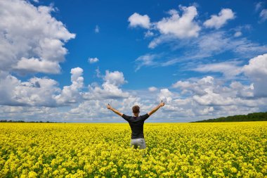 Attractive man with arms outstretched. Handsome young man standing in a field of blooming yellow rapeseed flowers.