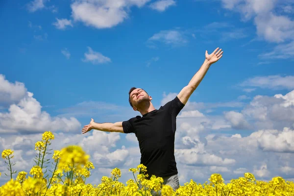 Attractive man with arms outstretched. Handsome young man standing in a field of blooming yellow rapeseed flowers.