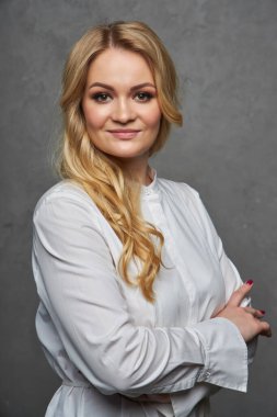 Portrait of an attractive woman, shot in the studio against a grey background, arms crossed on chest