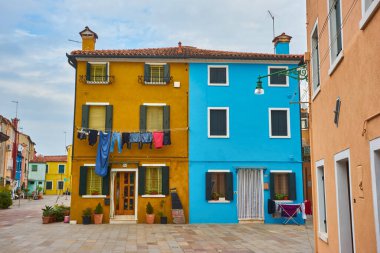 Kuzey İtalya 'daki Burano adasındaki güzel renkli ev cephesi. Yarı turuncu, yarı mavi, sarı kapılı ve içinde bitkiler olan iki pencereli ev duvarı.