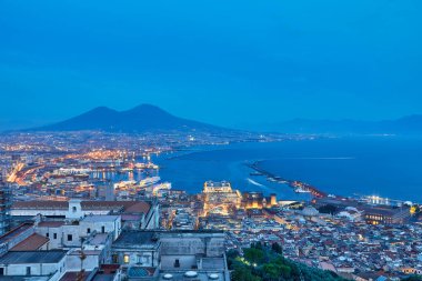 Vomero bölgesinden Napoli 'nin gece görüşü. Castel Sant 'elmo ön planda, arka planda şehrin limanı ve Ovo kalesi. Evler ve binalar var..